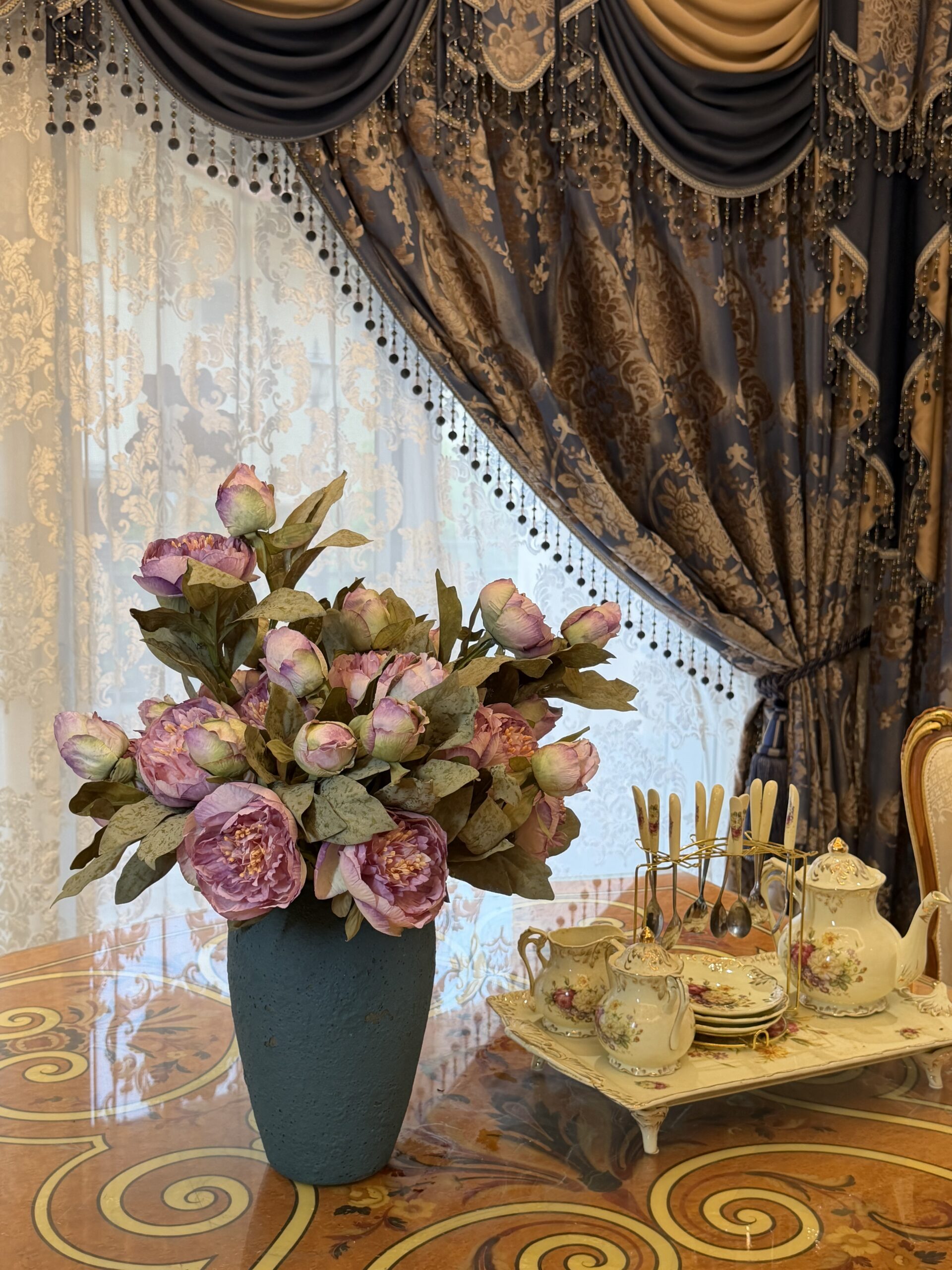Pink artificial peony arrangement displayed beside a vintage tea set