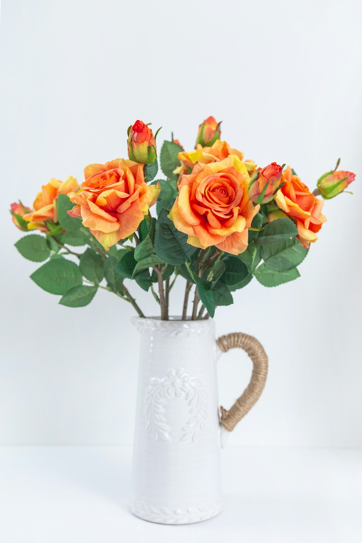 Artificial orange flowers in a white vase displayed in a bright room